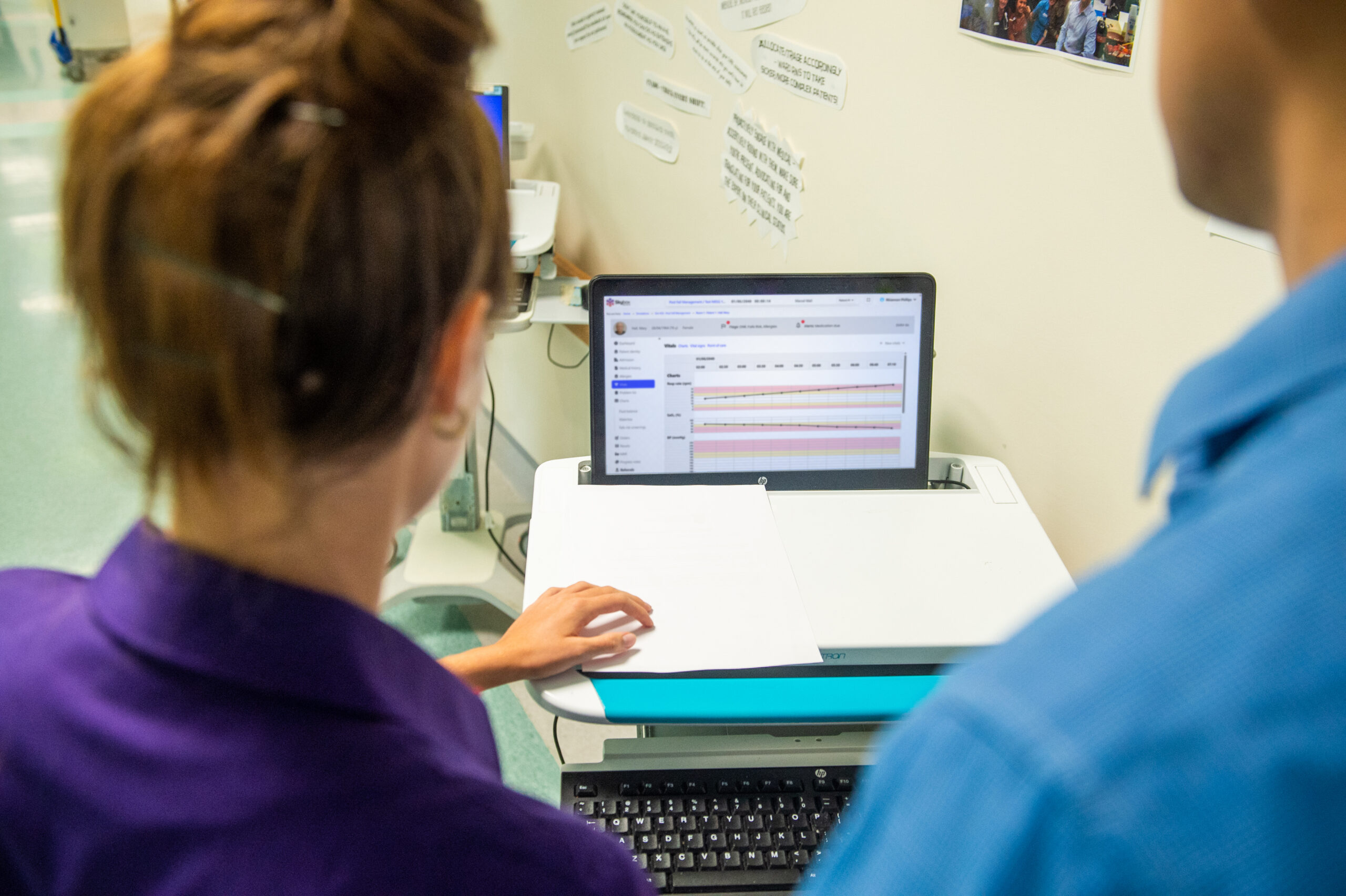 Two students seen from behind looking at the vitals page of an academic electronic medical record.